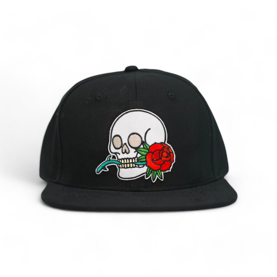 A black snapback cap with a graphic of a skull and a rose on the front.