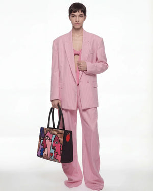 Person wearing a pink suit holding a colorful bag on a white background