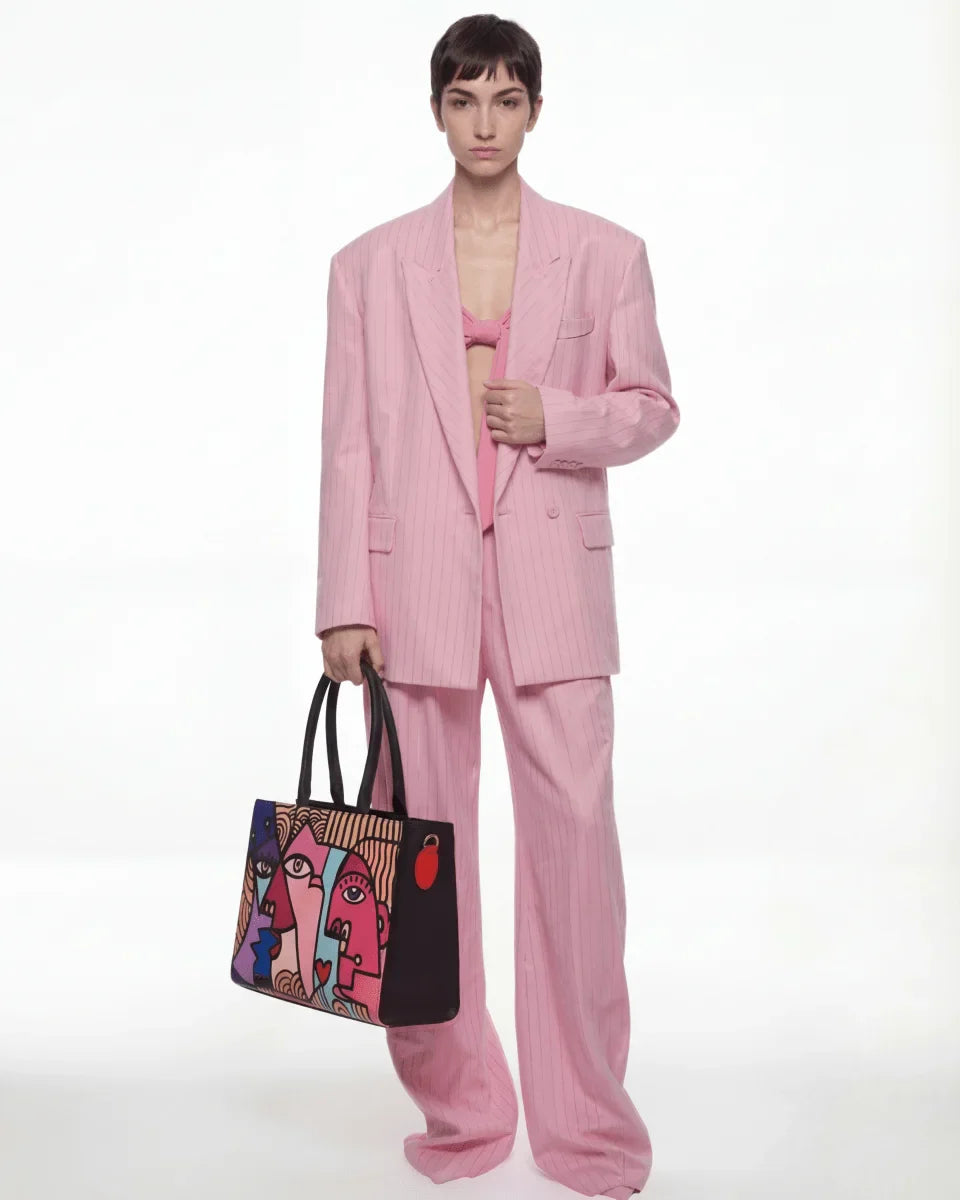 Person wearing a pink suit holding a colorful bag on a white background