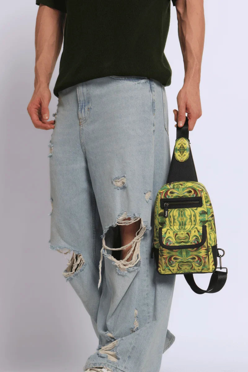 Full product view of a Person wearing ripped jeans holding a Kosmic Immersion Helios sling bag for men against a white background